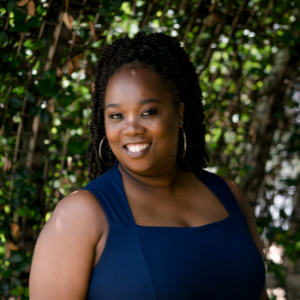 black woman standing outside smiling wearing navy blue top